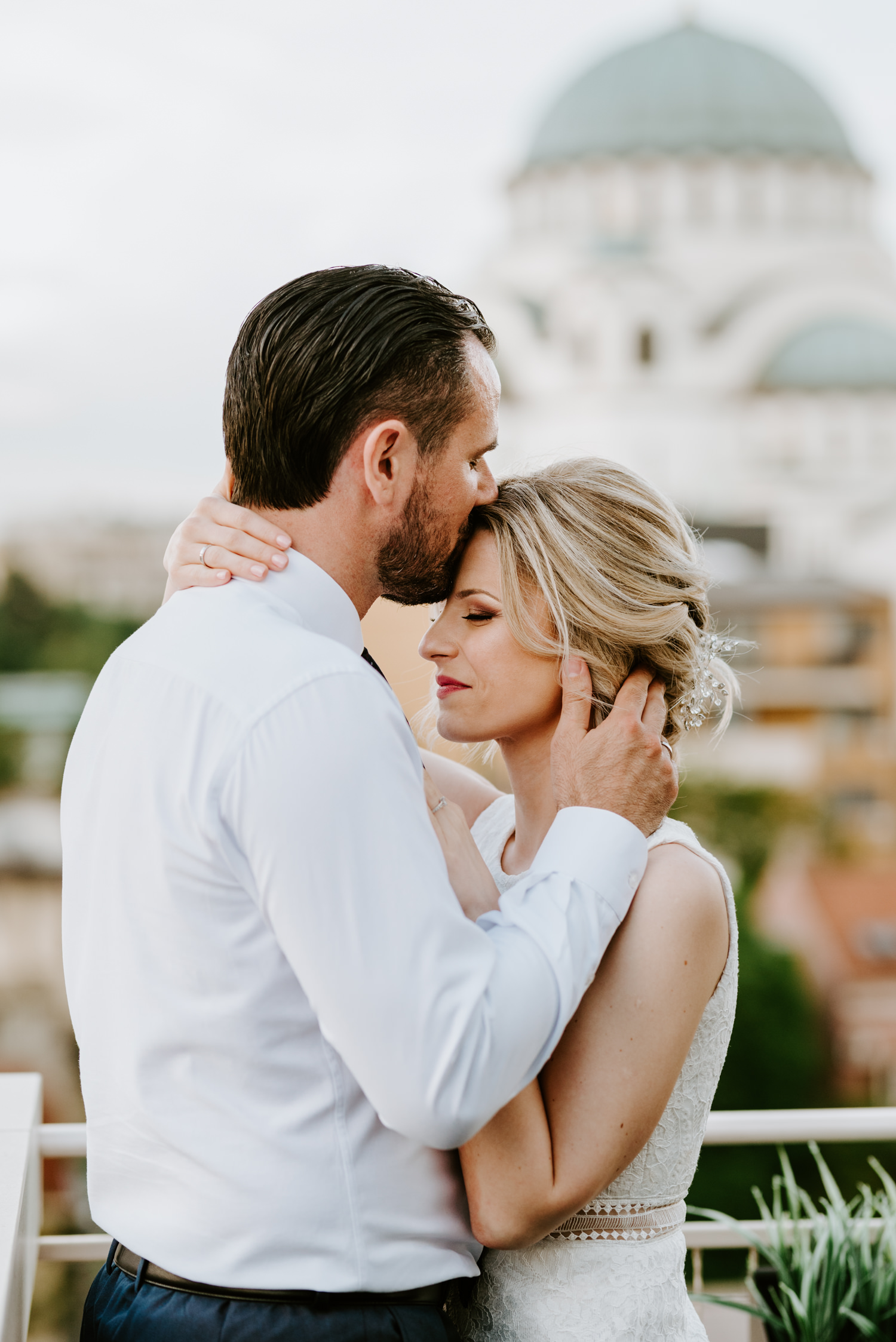 Mladoženja ljubi mladu u čelu na terasi Chrystall rooftop restorana sa pogledom na hram svetog Save